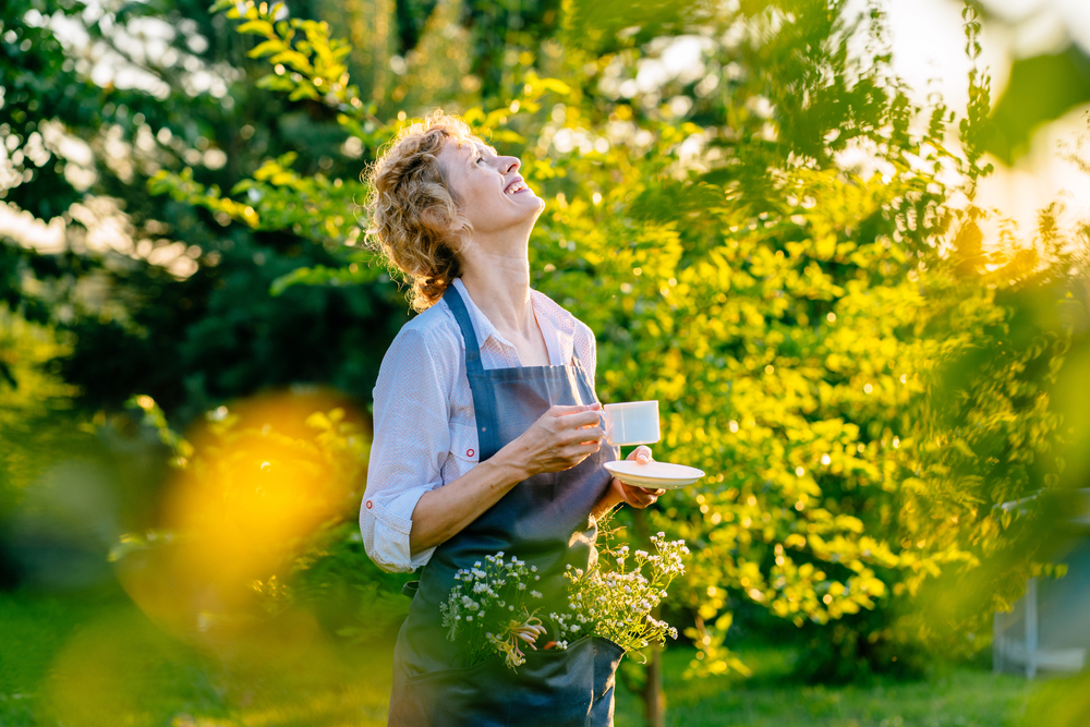 Glad kvinna som dricker kaffe i trädgården

